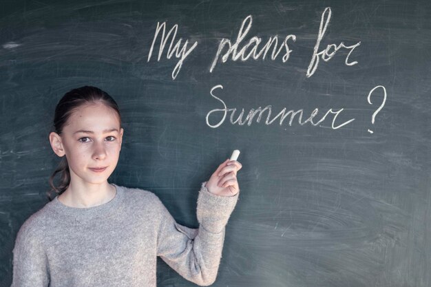 Photo portrait d'une fille tenant une craie par texte sur le tableau noir en classe