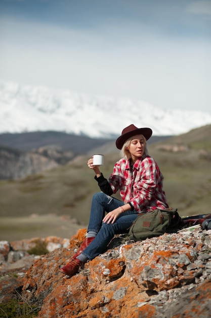 Photo portrait de fille voyageuse avec un chapeau et une tasse sur le fond des montagnes