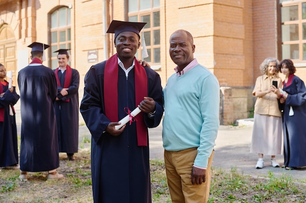 Portrait de fils en robe de graduation souriant à la caméra avec son père