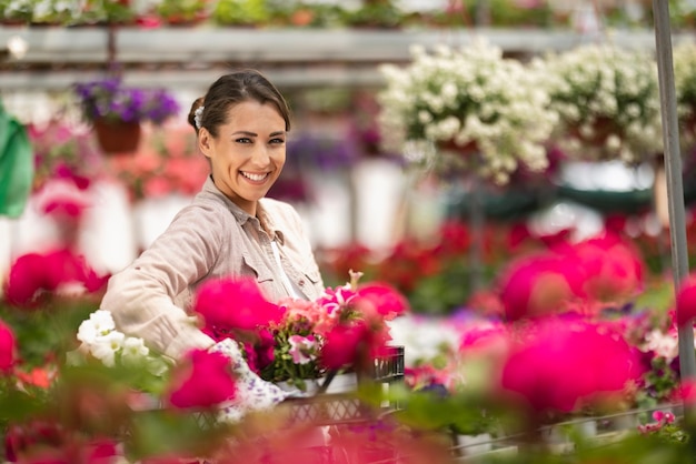 Portrait de fleuriste belle femme dans une serre. Elle tient une caisse avec de belles fleurs et regarde la caméra.