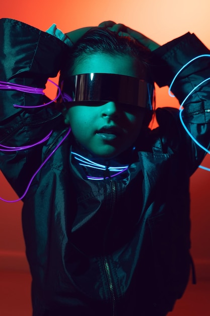 Portrait flou enfant garçon cyberpunk dans des lunettes vr dans des tons bleus et rouges avec des fils sur fond rouge