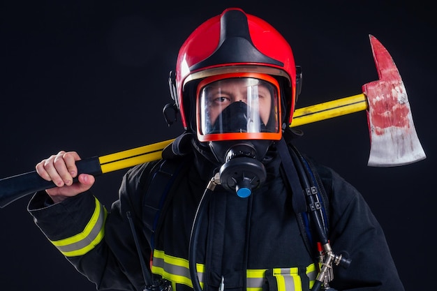 Portrait fort pompier en uniforme ignifuge tenant une hache dans ses mains fond noir studio