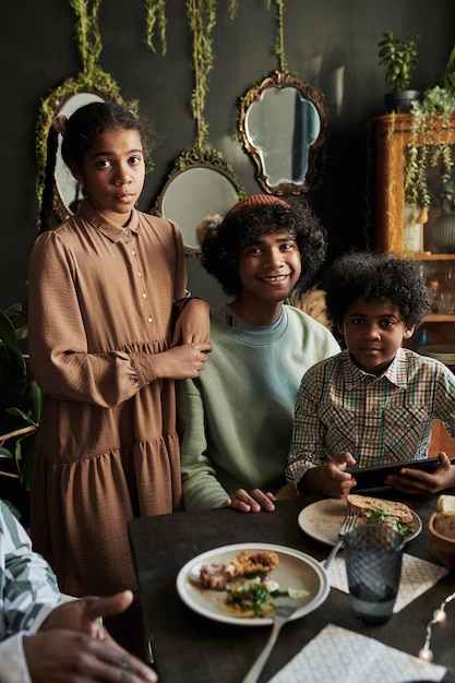 Portrait de frères heureux avec leur sœur souriant à la caméra tout en dînant avec la famille à la maison