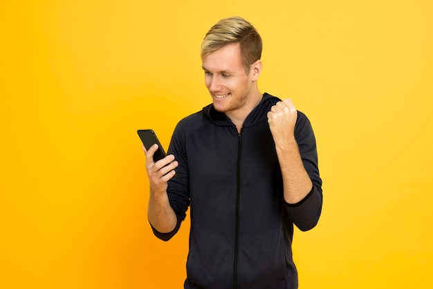 Portrait gai jeune homme jouant un téléphone portable isolé sur fond jaune