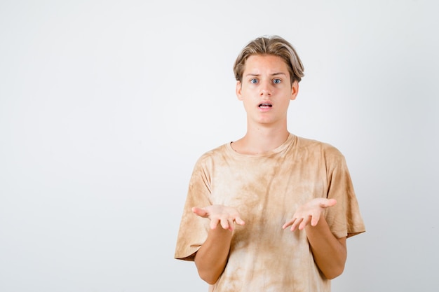 Portrait d'un garçon adolescent faisant un geste de question en t-shirt et à la vue de face perplexe