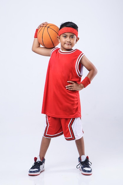 Portrait d'un garçon asiatique dans un maillot rouge tenant un ballon de basket