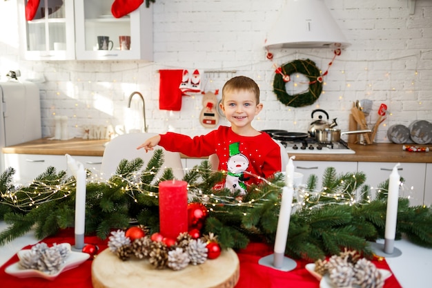 Un portrait d'un garçon assis dans la cuisine à la table de Noël, qui est décorée pour la nouvelle année. Déco de Noël dans la cuisine