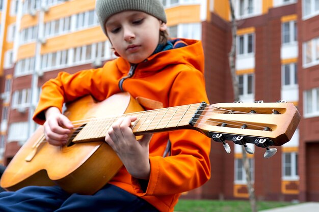 Photo portrait d'un garçon blond caucasien en veste orange jouant de la guitare acoustique à l'extérieur un jour d'automne