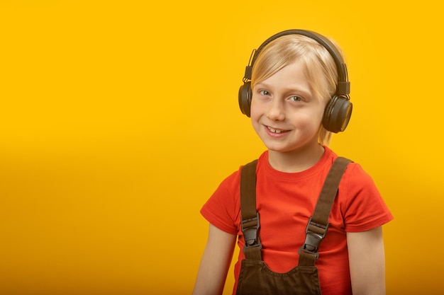 Portrait d'un garçon blond dans un casque sur fond jaune Enfant écoute de la musique en souriant et en regardant dans l'espace de copie de l'appareil photo