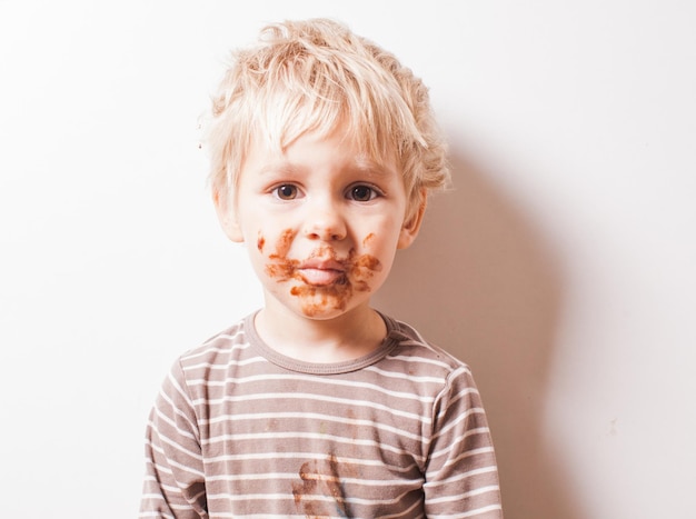 Portrait d'un garçon blond avec du chocolat sur son visage isolé sur blanc