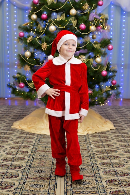 Portrait d'un garçon en costume de Père Noël près de l'arbre de Noël