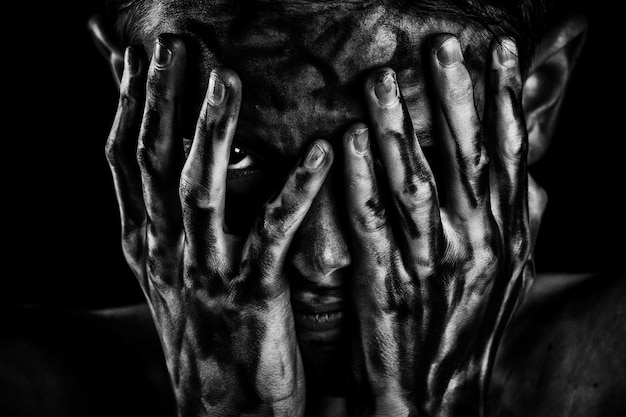 Portrait d'un garçon couvrant le visage avec les mains sur un fond noir
