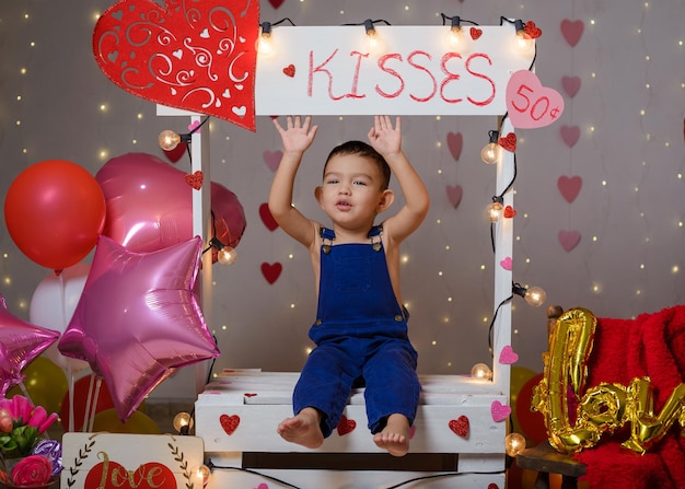 Portrait d'un garçon dans une cabine de baisers décorée de coeurs et de ballons