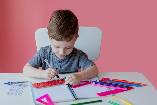 Portrait de garçon enfant mignon à la maison à faire ses devoirs. Petit enfant concentré écrivant avec un crayon coloré, à l'intérieur.