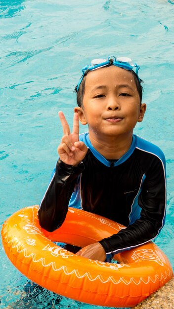 Photo portrait d'un garçon faisant un signe de paix en nageant dans une piscine