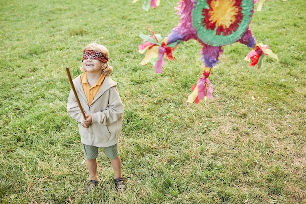 Portrait de garçon jouant au jeu de pinata lors d'une fête d'anniversaire à l'extérieur et tenant un espace de copie de chauve-souris