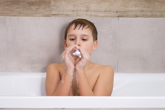 Portrait d'un garçon jouant avec du shampoing ou du gel dans la salle de bain, un enfant se baigne et gonfle des bulles de savon