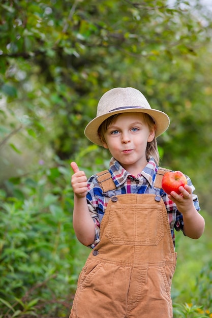 Portrait d'un garçon mignon dans un chapeau dans le jardin avec une pomme rouge émotions bonheur nourriture récolte d'automne