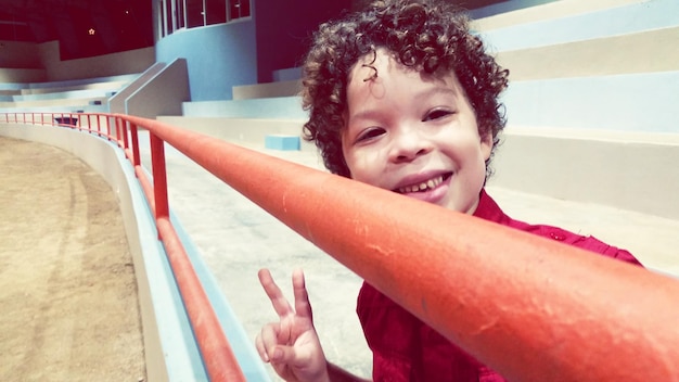 Portrait d'un garçon mignon faisant des gestes de signe de paix par la balustrade au stade