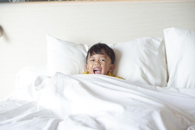 Portrait d'un garçon souriant allongé et portant une couverture sur le lit en regardant la télévision