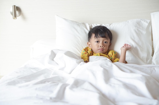 Portrait d'un garçon souriant allongé et utilisant une couverture sur le lit tout en regardant la télévision