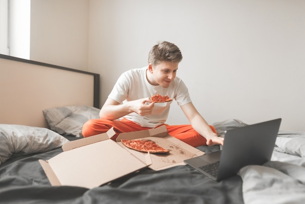 Portrait d'un garçon souriant assis sur un lit avec une boîte de pizza