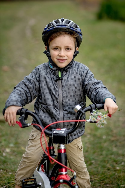 Portrait de garçon souriant dans un casque avec un vélo dans le parc.
