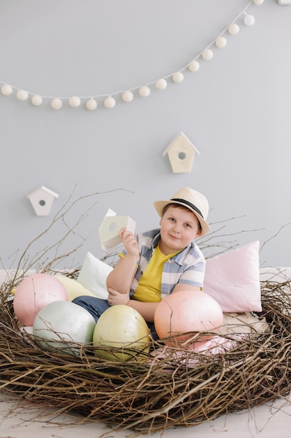 Portrait d'un garçon souriant dans un chapeau dans un nid décoratif de Pâques avec des oeufs de Pâques, des branches de saule sèches.