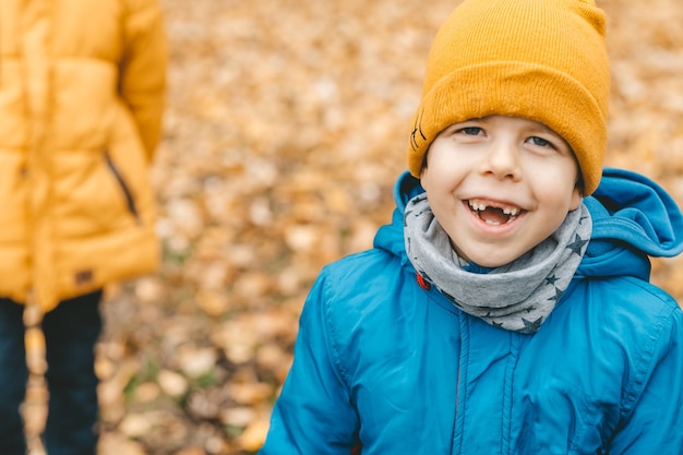 Portrait d'un garçon souriant dans un chapeau et une veste bleue, à l'extérieur, sur fond de congé jaune. Beau et mignon garçon souriant en regardant dans le cadre. heureux enfant édenté riant dans le cadre