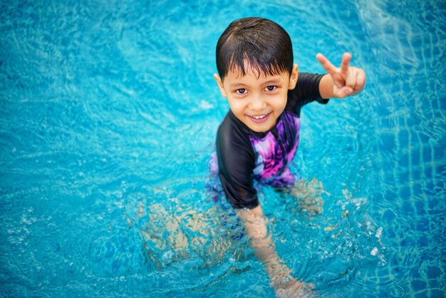 Photo portrait d'un garçon souriant faisant des gestes alors qu'il se tient dans la piscine