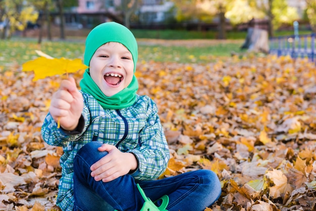 Portrait de garçon souriant heureux avec feuille d'érable à l'extérieur