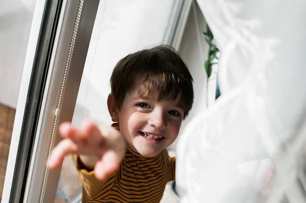Portrait d'un garçon souriant qui tend la main alors qu'il se tient à la maison