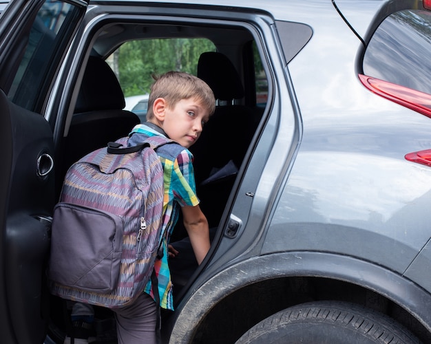 Portrait de garçon souriant avec sac d'école de perdre en voiture. Prendre un élève après l'école. Le garçon monte dans la voiture.