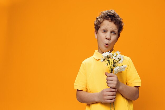 Portrait d'un garçon tenant une fleur alors qu'il se tient contre un fond jaune