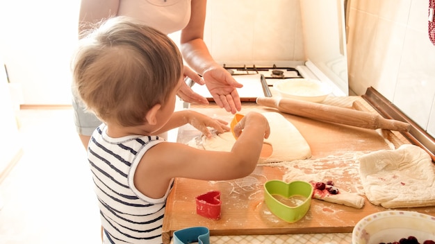 Portrait d'un garçon tout-petit souriant et heureux avec une jeune mère qui prépare et cuisine dans la cuisine. Parent enseignant et éduquant l'enfant à la maison