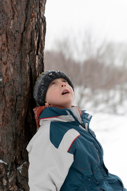 Portrait de garçon en vêtements d'hiver près de l'arbre sur fond de parc d'hiver. Promenez-vous dans le parc d'hiver.