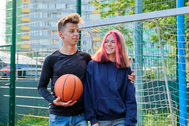 Portrait d'un gars et d'une adolescente étreignant sur un terrain de basket avec un ballon dans les mains