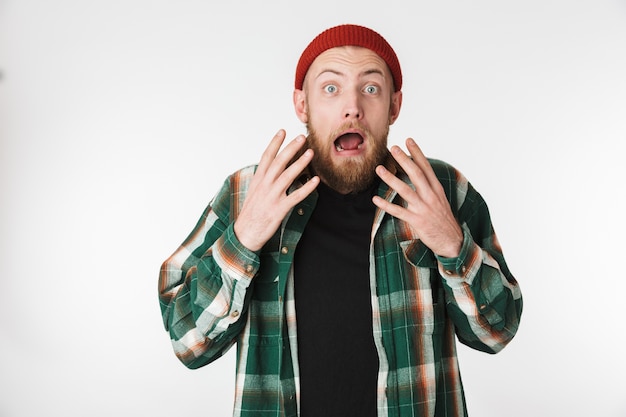 Portrait de gars barbu émotionnel portant chapeau et chemise à carreaux souriant, tout en se tenant isolé sur fond blanc