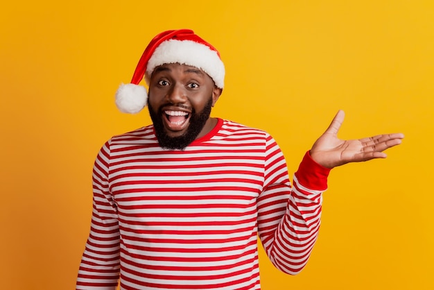 Portrait d'un gars en bonnet de noel visage fou tenir la paume des gestes sur fond jaune