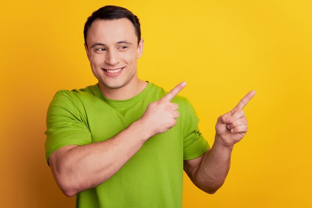 Portrait d'un gars curieux qui fait la promotion de l'espace vide du doigt sur le côté du regard sur fond jaune