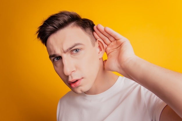 Portrait d'un gars curieux regarde l'oreille de la main de la caméra espionnage sur fond jaune