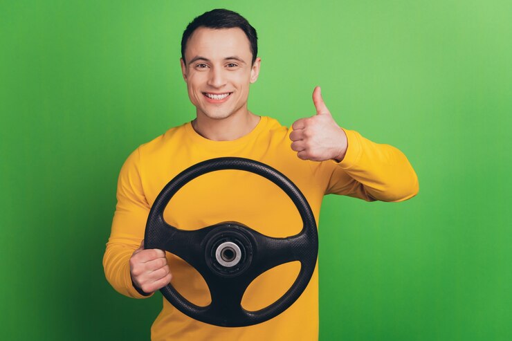Portrait d'un gars fiable et positif tenir le volant lever le pouce vers le haut sur fond vert