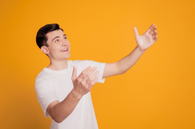 Portrait d'un gars inspiré rêveur drôle qui s'étire la main attrape les mains espace vide sur fond jaune