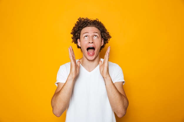 Portrait de gars joyeux aux cheveux bruns bouclés hurlant et levant les mains pour faire face