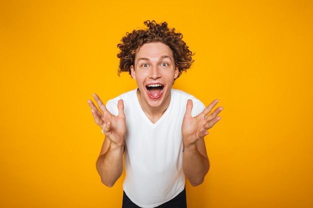 Portrait de gars positif avec des cheveux bruns bouclés crier avec lever les mains pour faire face