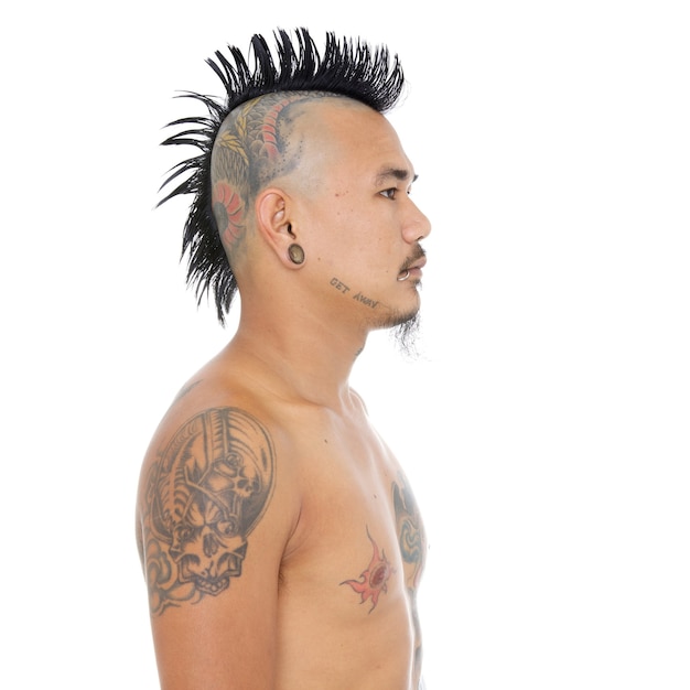 Portrait d'un gars punk asiatique avec une coiffure mohawk, un tatouage de tête, un piercing aux lèvres et aux oreilles isolé sur fond blanc