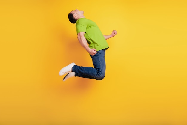 Portrait d'un gars sportif fou et étonné qui saute s'amuser sur un mur jaune