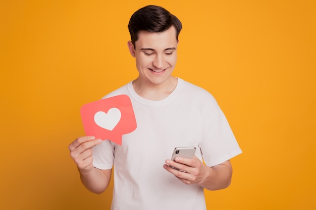 Portrait d'un gars tenir un téléphone portable comme une carte postale en train de discuter avec un écran d'apparence sourire à pleines dents sur fond jaune