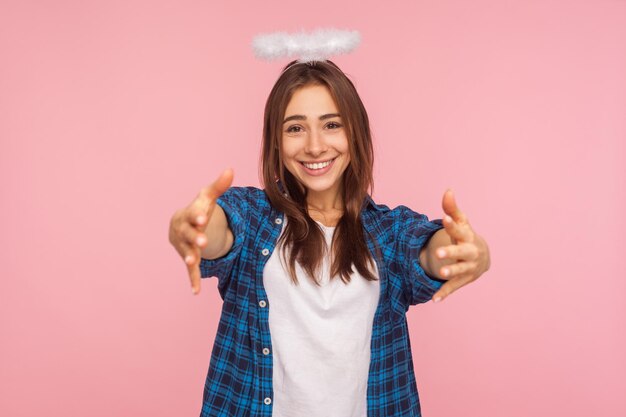 Portrait d'une gentille fille positive avec un nimbus au-dessus de la tête étirant les bras vers la caméra avec un sourire amical et généreux, allant embrasser, partager l'amour et les soins. studio d'intérieur tourné isolé sur fond rose