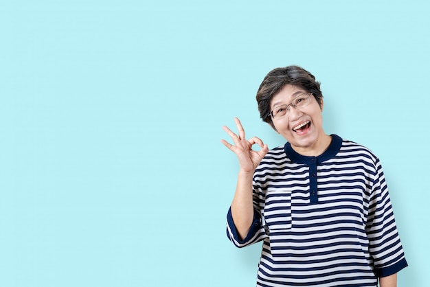 Portrait de geste de femme asiatique senior heureuse ou montrant la main ok et regardant la caméra